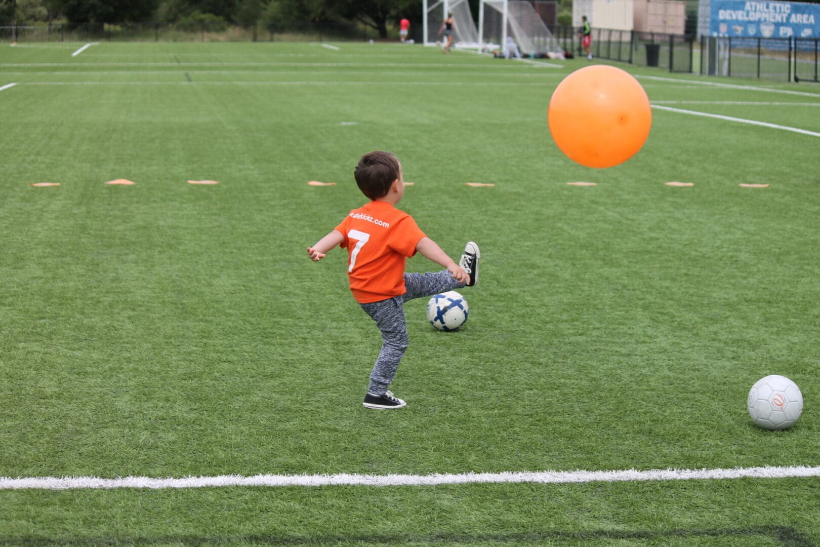 A young boy kicking around an orange ball on the soccer field.